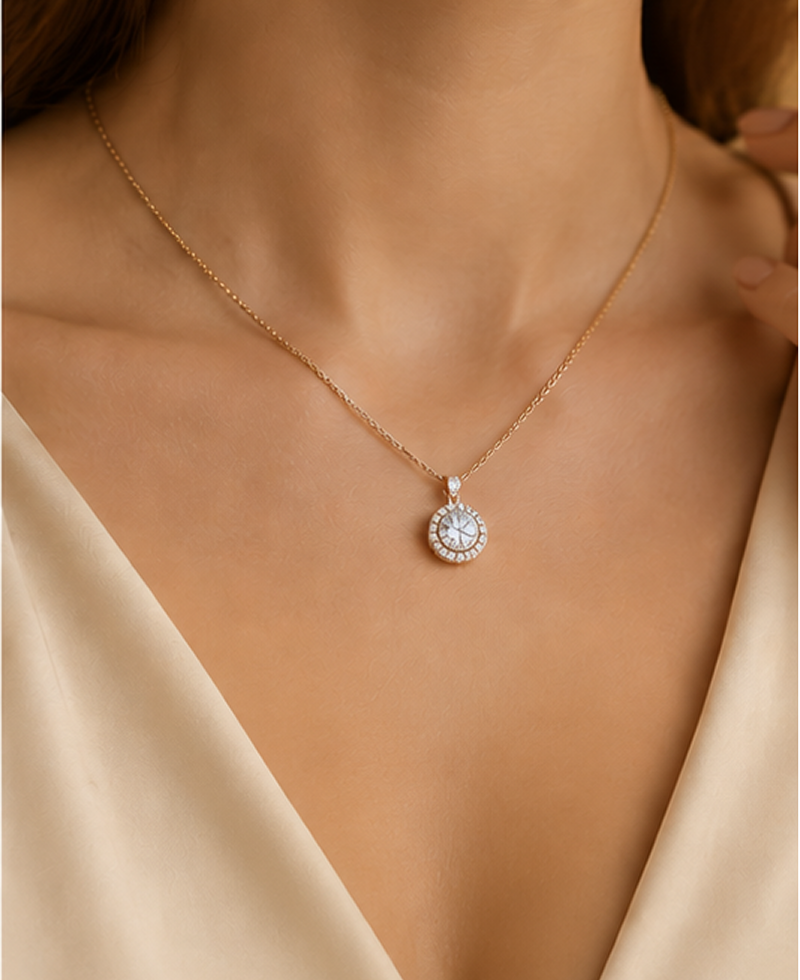 A close-up of a model wearing a delicate gold chain necklace with a round halo pendant set with clear stones, styled with a cream satin top.2